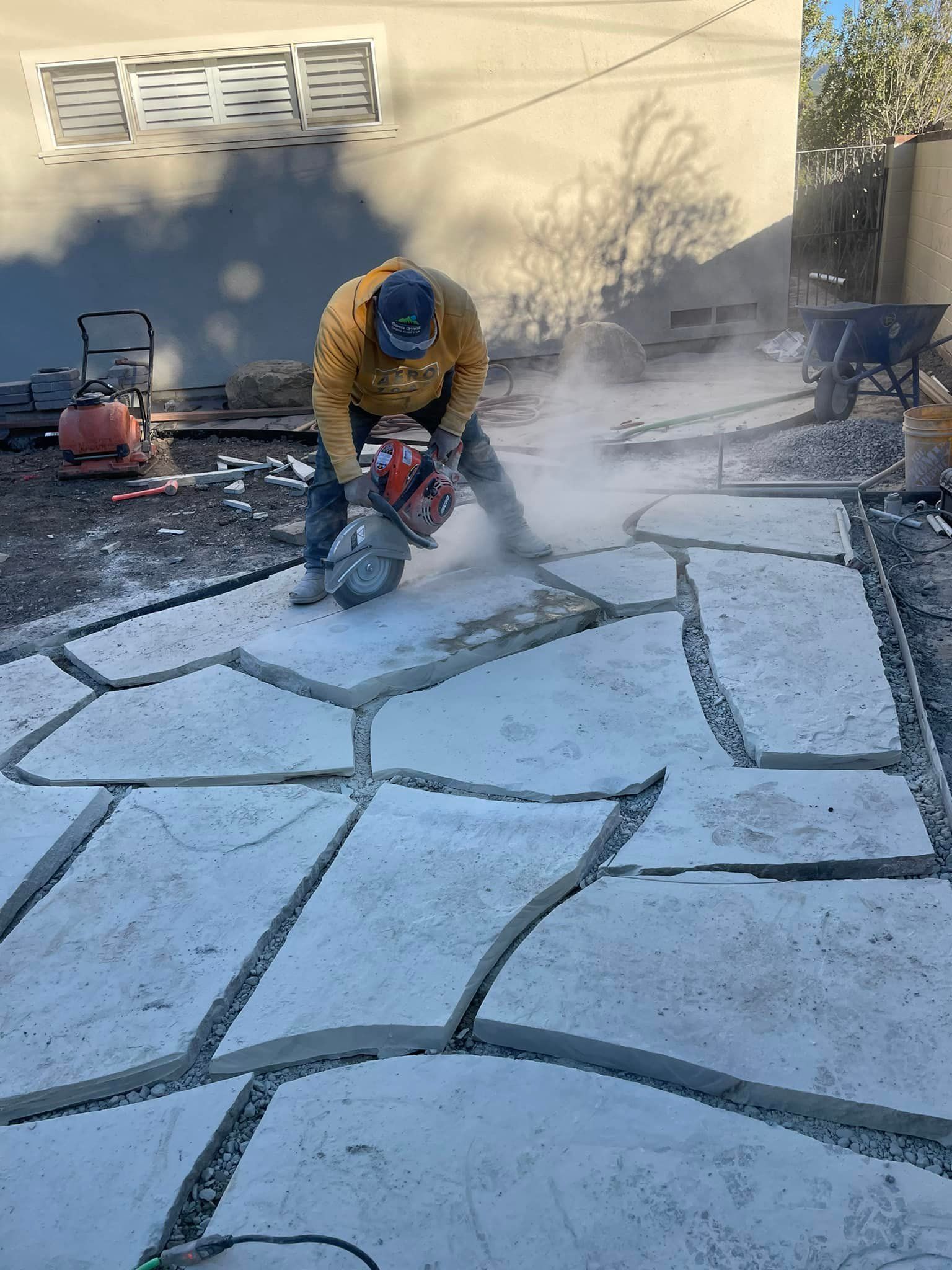 A man is cutting concrete with a chainsaw on a patio.