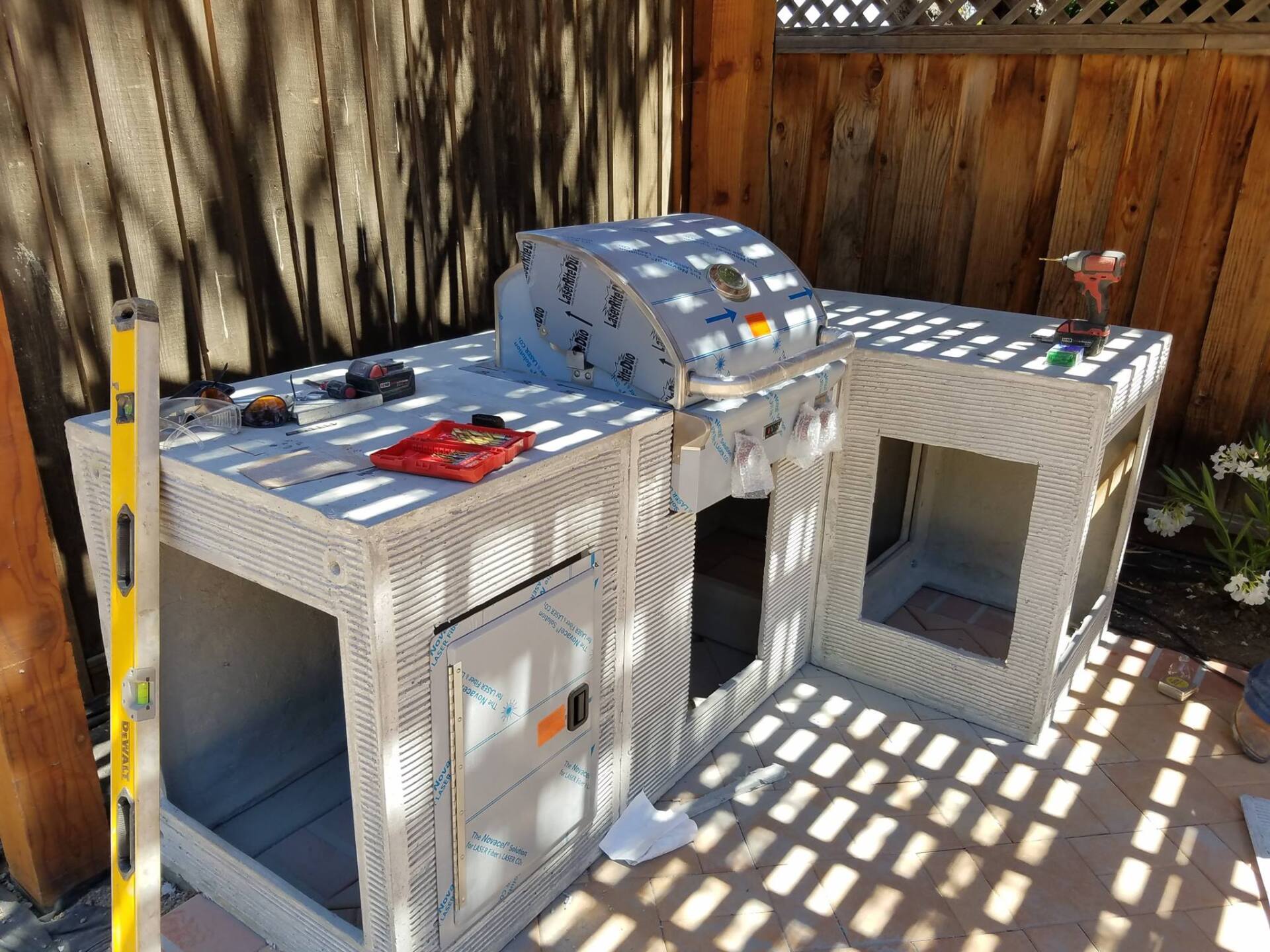 A bbq grill is being built on a patio next to a wooden fence.