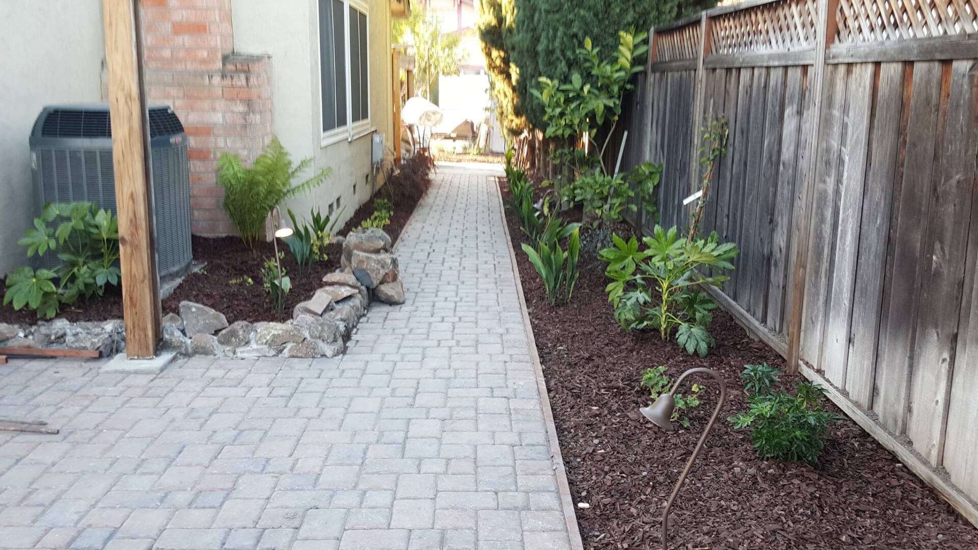 A brick walkway leading to a house with a wooden fence.