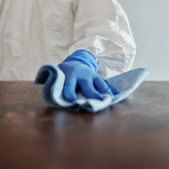 A pereson wearing a protective suit and gloves wipes a wood table