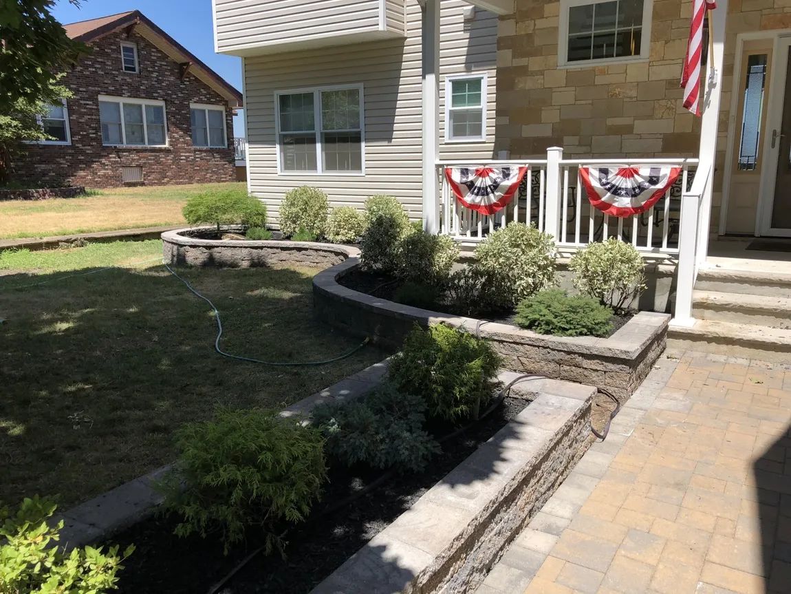 A house with a flag on the porch and a planter in front of it.