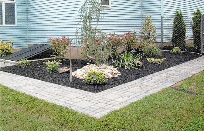 A brick walkway leading to a garden in front of a house.