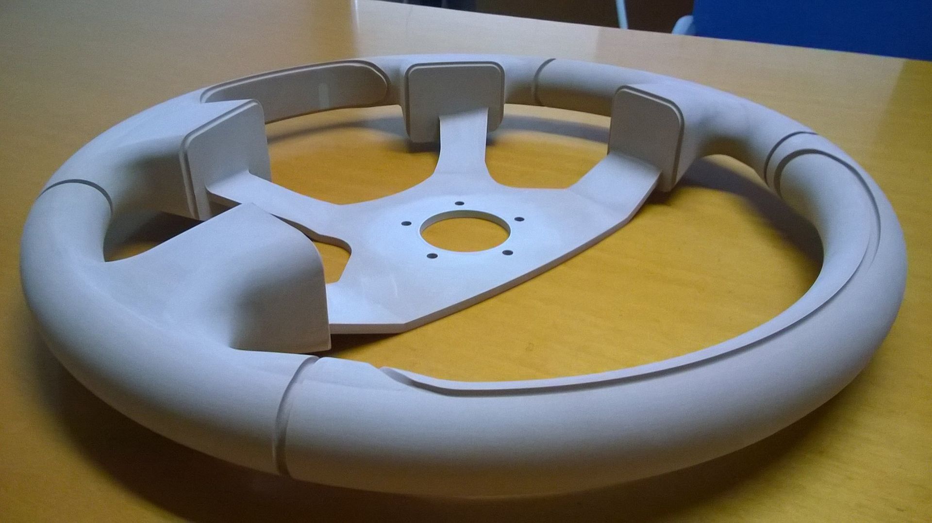 Volante marrone chiaro per auto con mozzo centrale e tre razze su un tavolo.