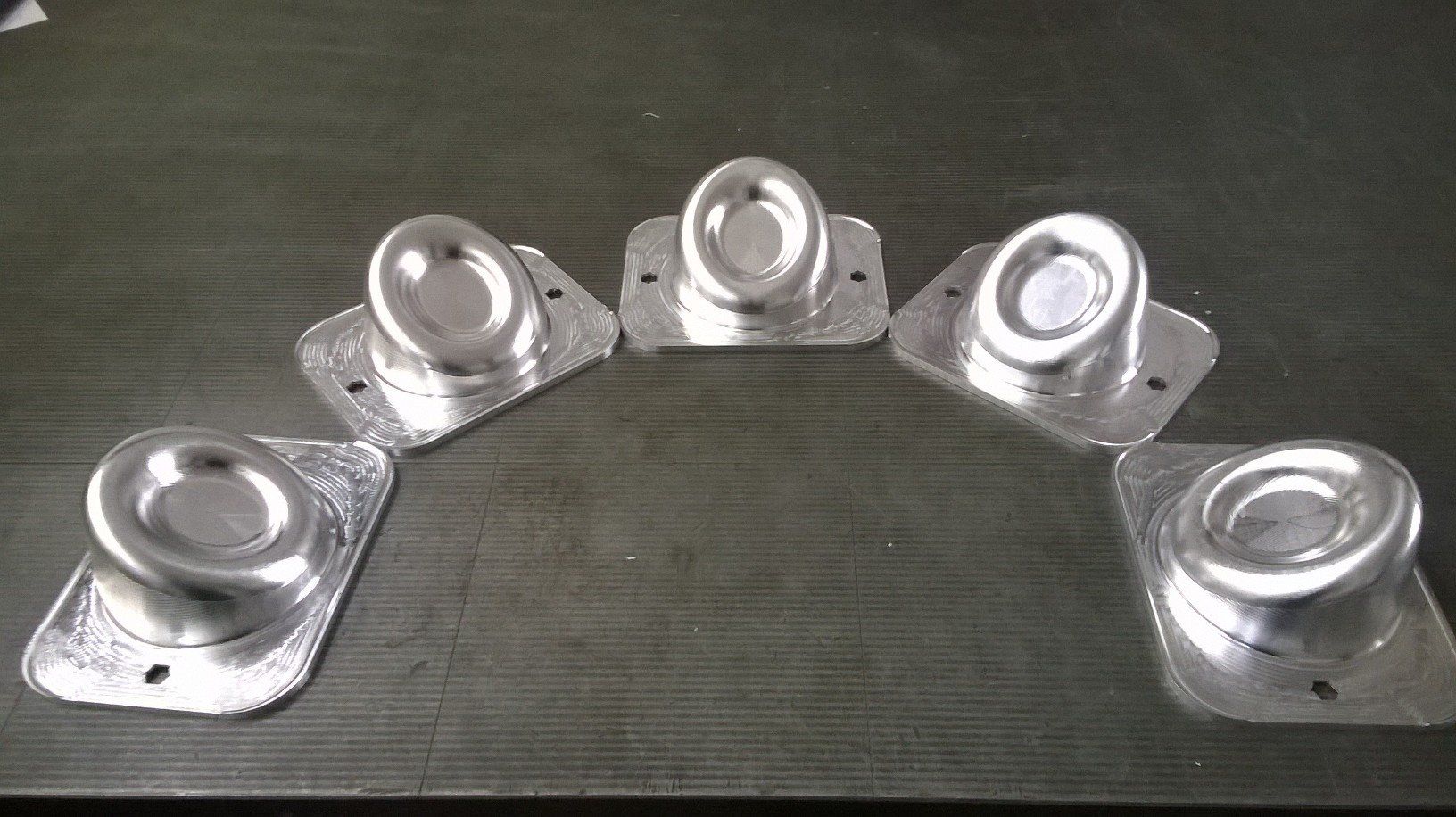 Cinque parti metalliche color argento disposte ad arco su una superficie scura, ciascuna con parte superiore arrotondata e piastra di montaggio.