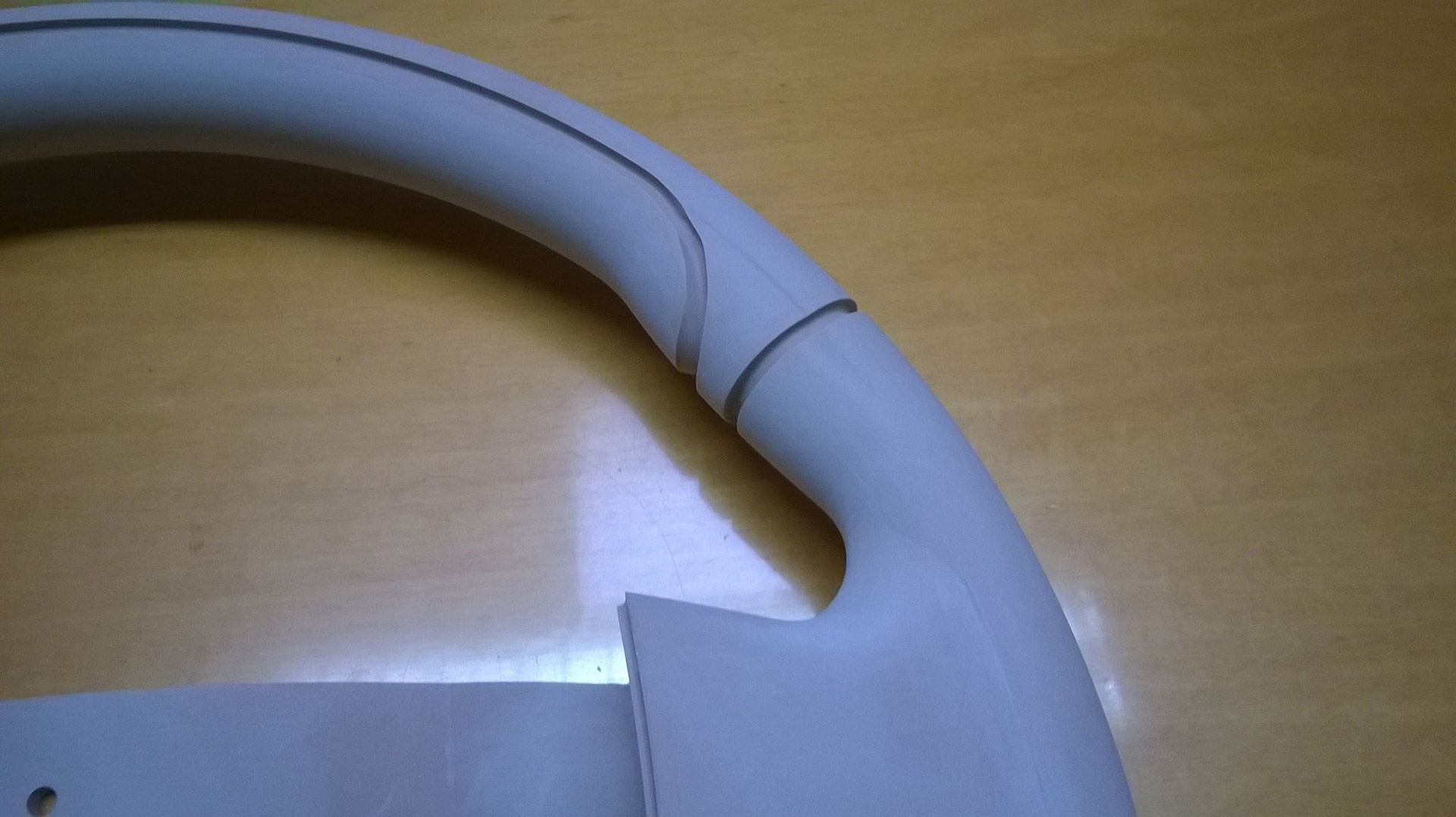 Primo piano del volante bianco di un'auto con cucitura e maniglia grigie, appoggiato su una superficie di legno.