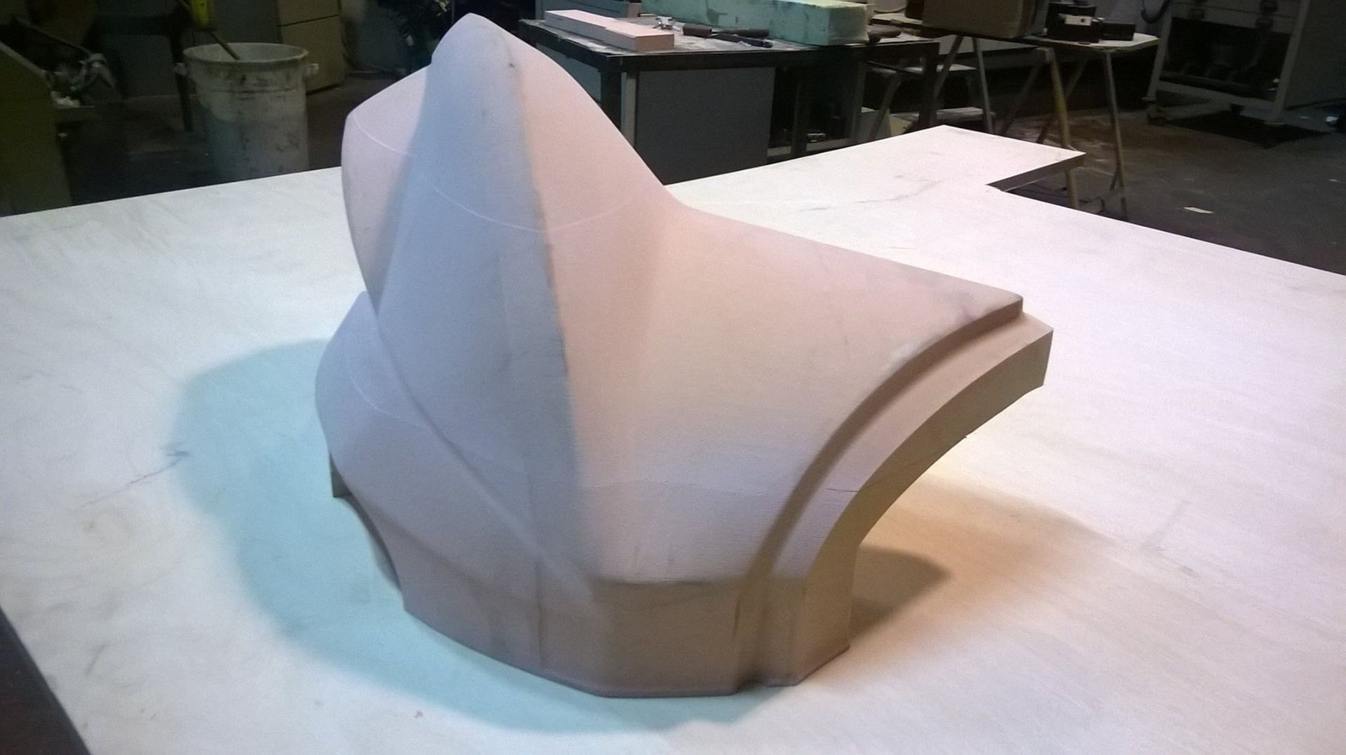 Un pezzo metallico lavorato con creste curve, posizionato su una base metallica, con un foro e la marcatura XY.