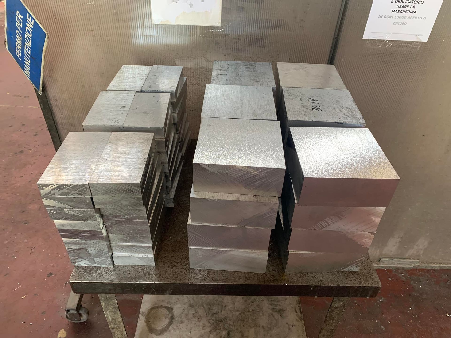 Pile di blocchi di metallo rettangolari su un carrello di metallo, probabilmente in un ambiente di fabbrica.