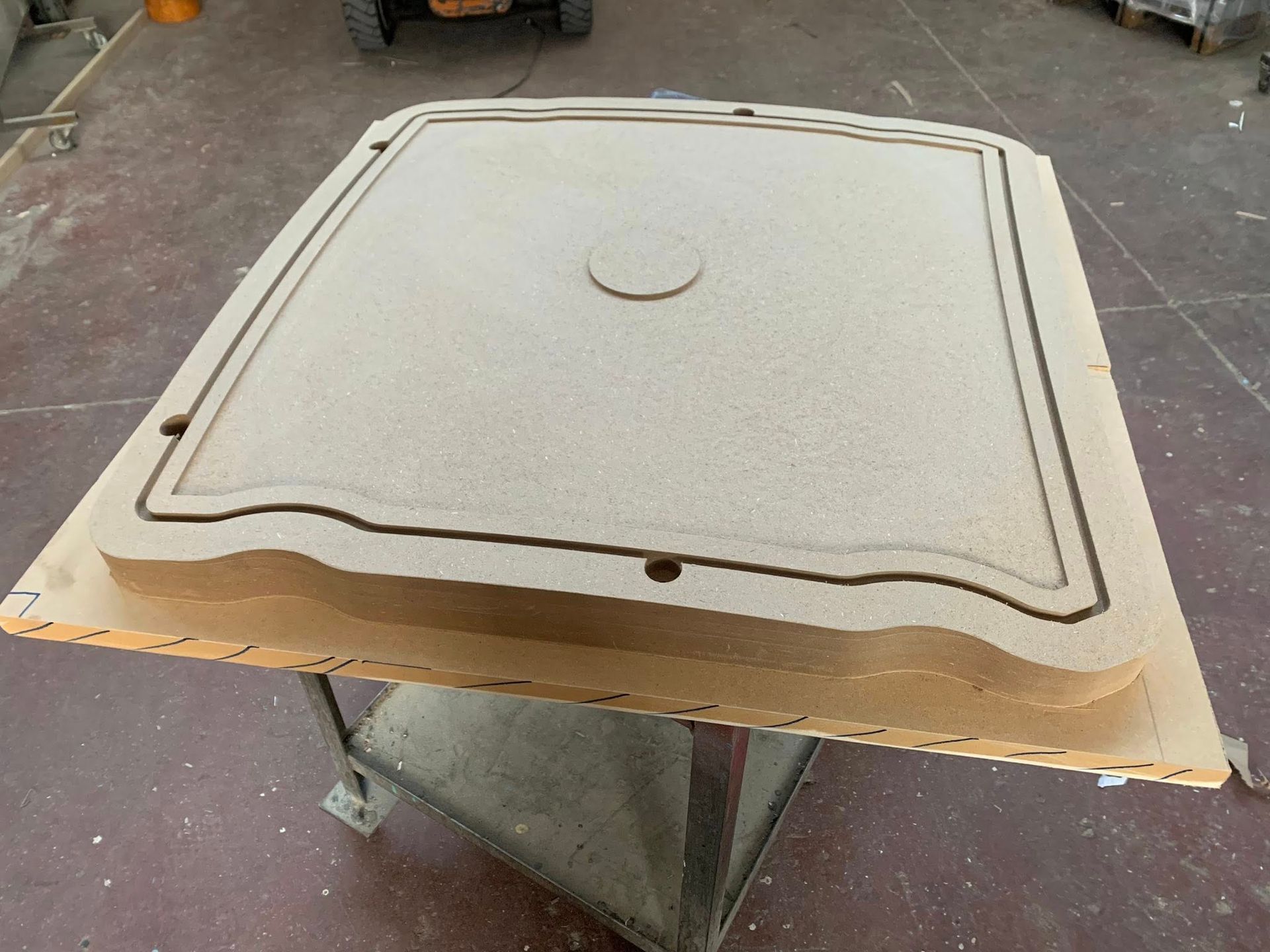 Un grande stampo in legno marrone chiaro con bordi curvi e un cerchio centrale, appoggiato su un supporto di metallo.