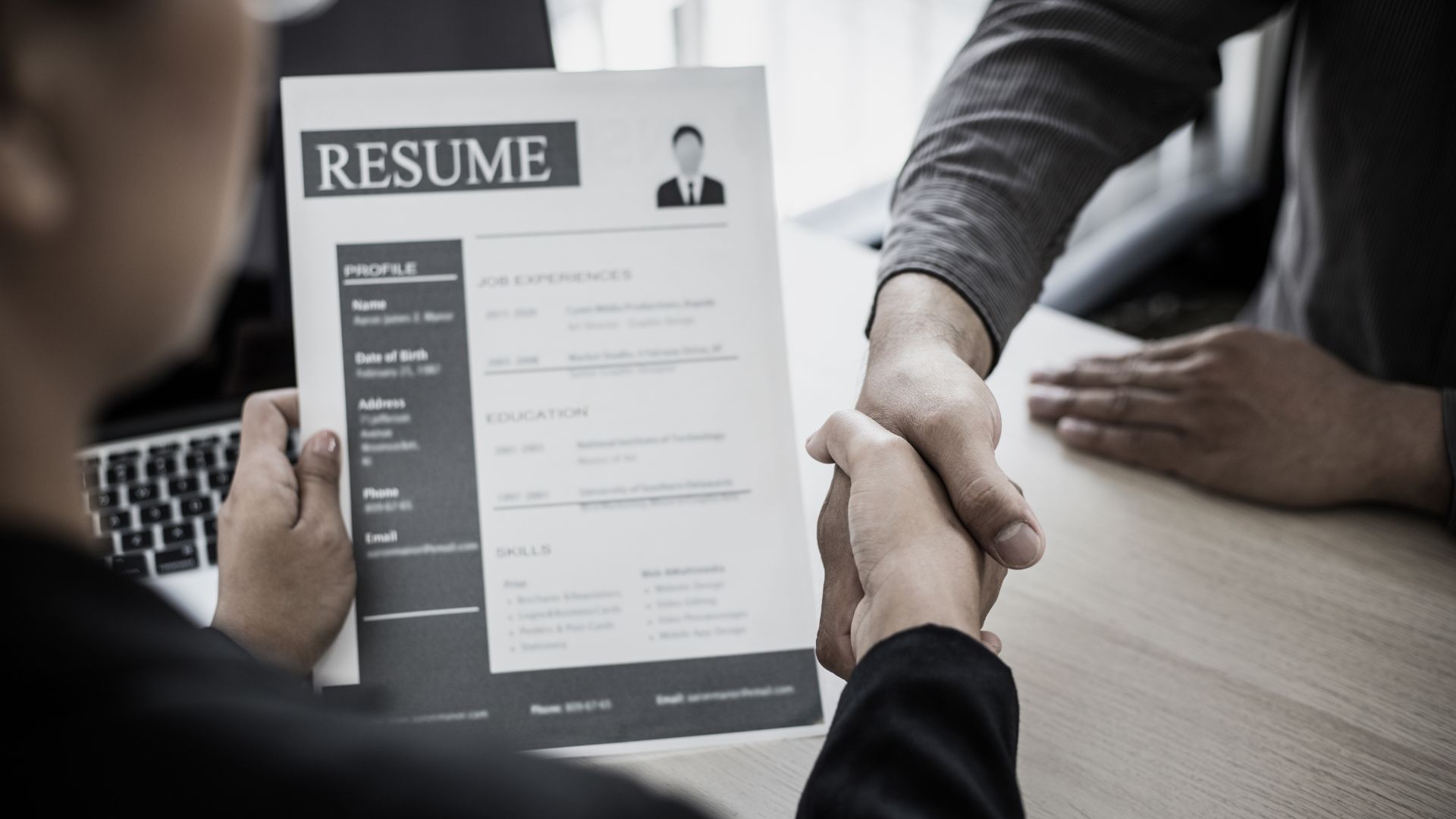 A man is shaking hands with a woman holding a resume.