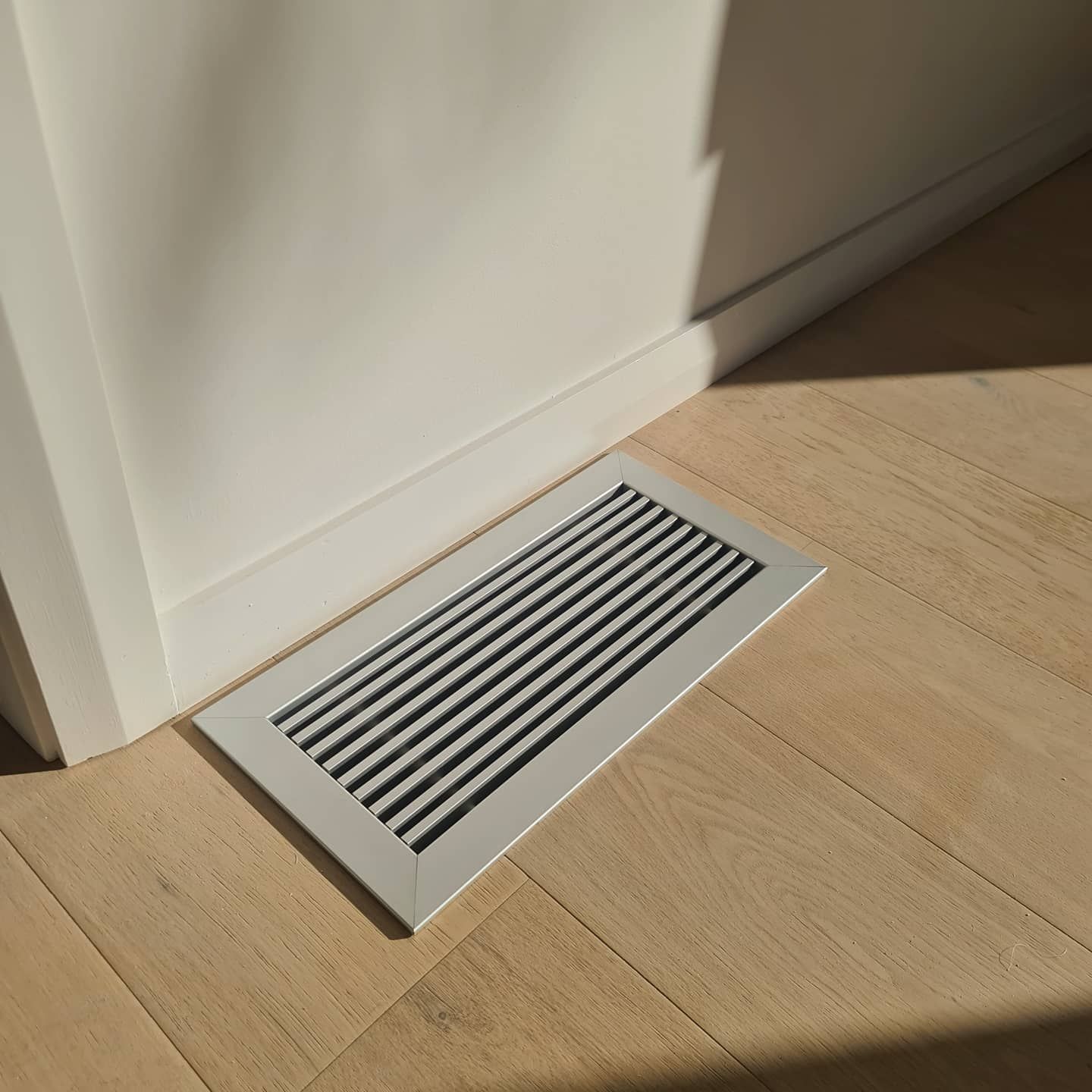 A white air vent is sitting on a wooden floor next to a door. — Coastline Air In Forresters Beach, NSW