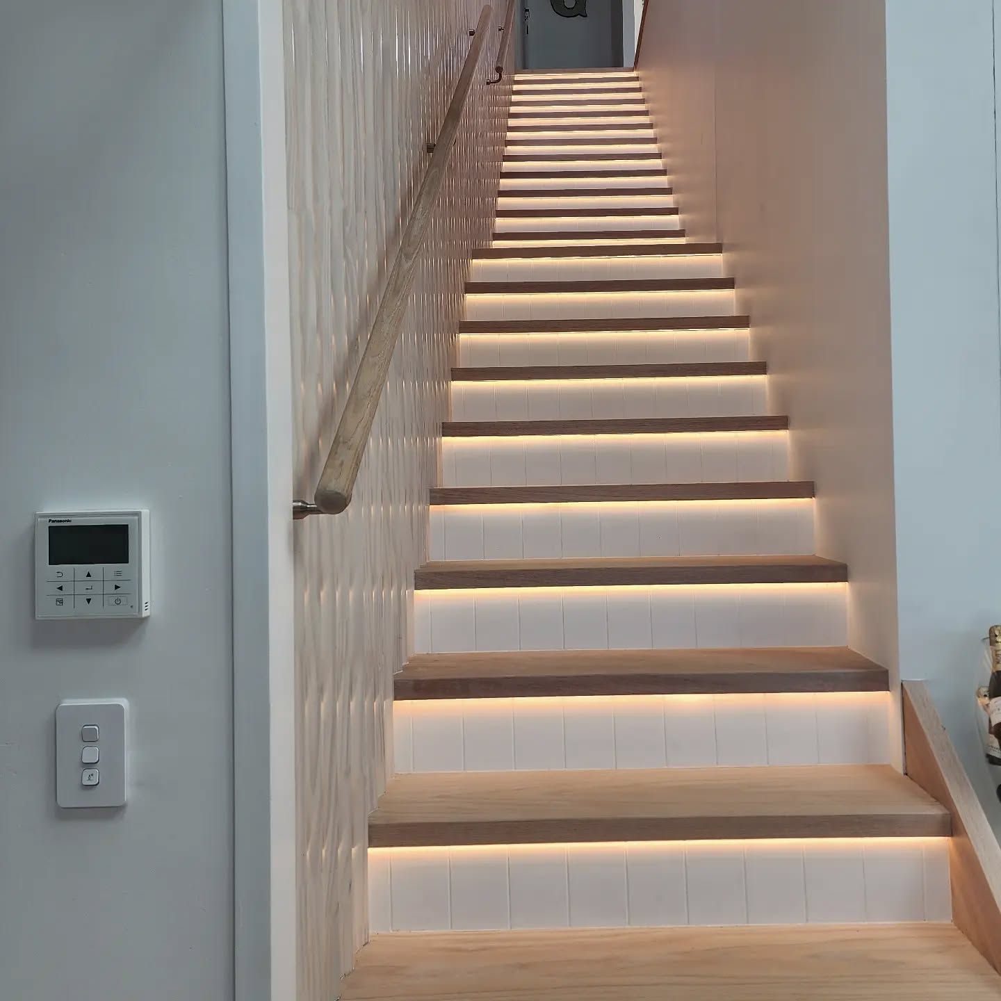 A staircase with lights on the steps and a remote control on the wall. — Coastline Air In Forresters Beach, NSW