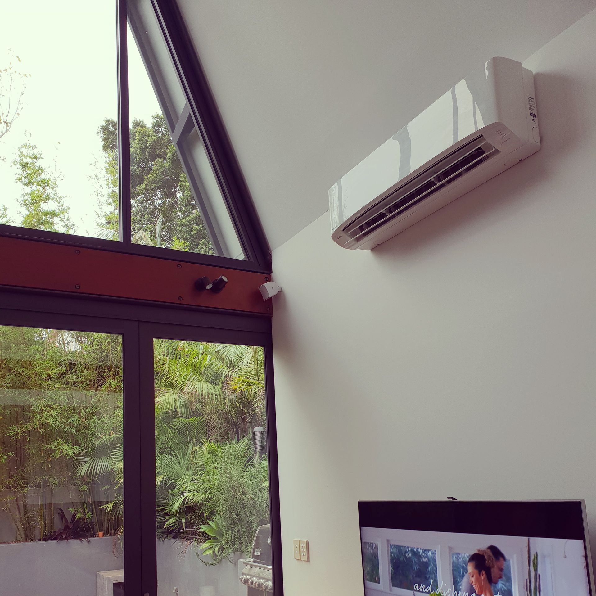 A TV is hanging on a wall next to a window — Coastline Air In Forresters Beach, NSW