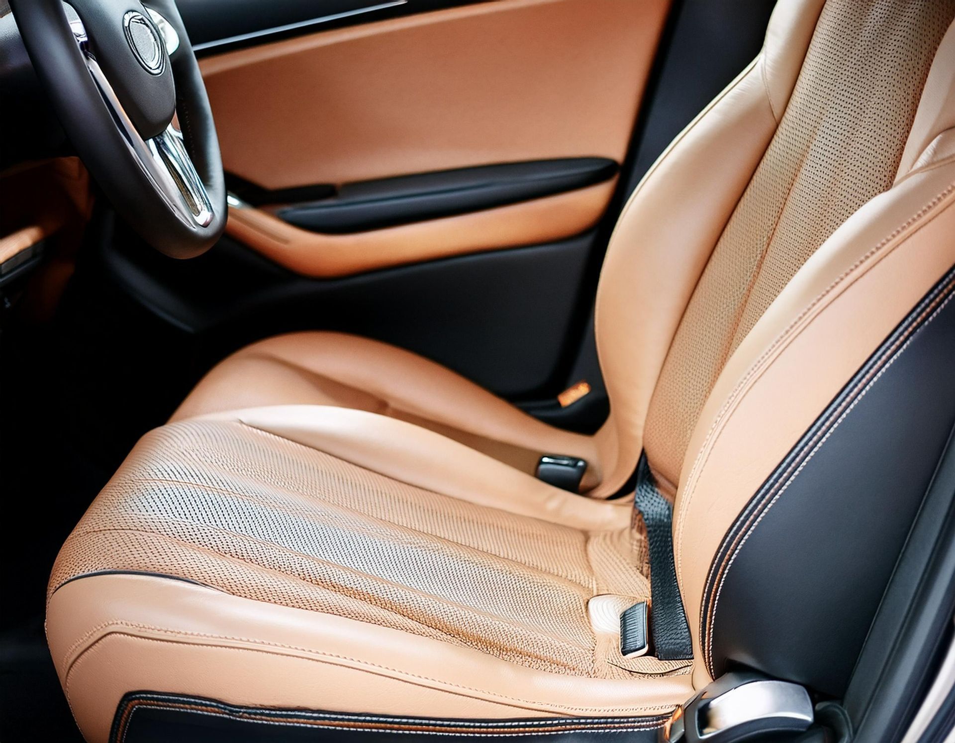 Beige leather car seat with significant wear and tear, adjacent to a black and tan door panel.