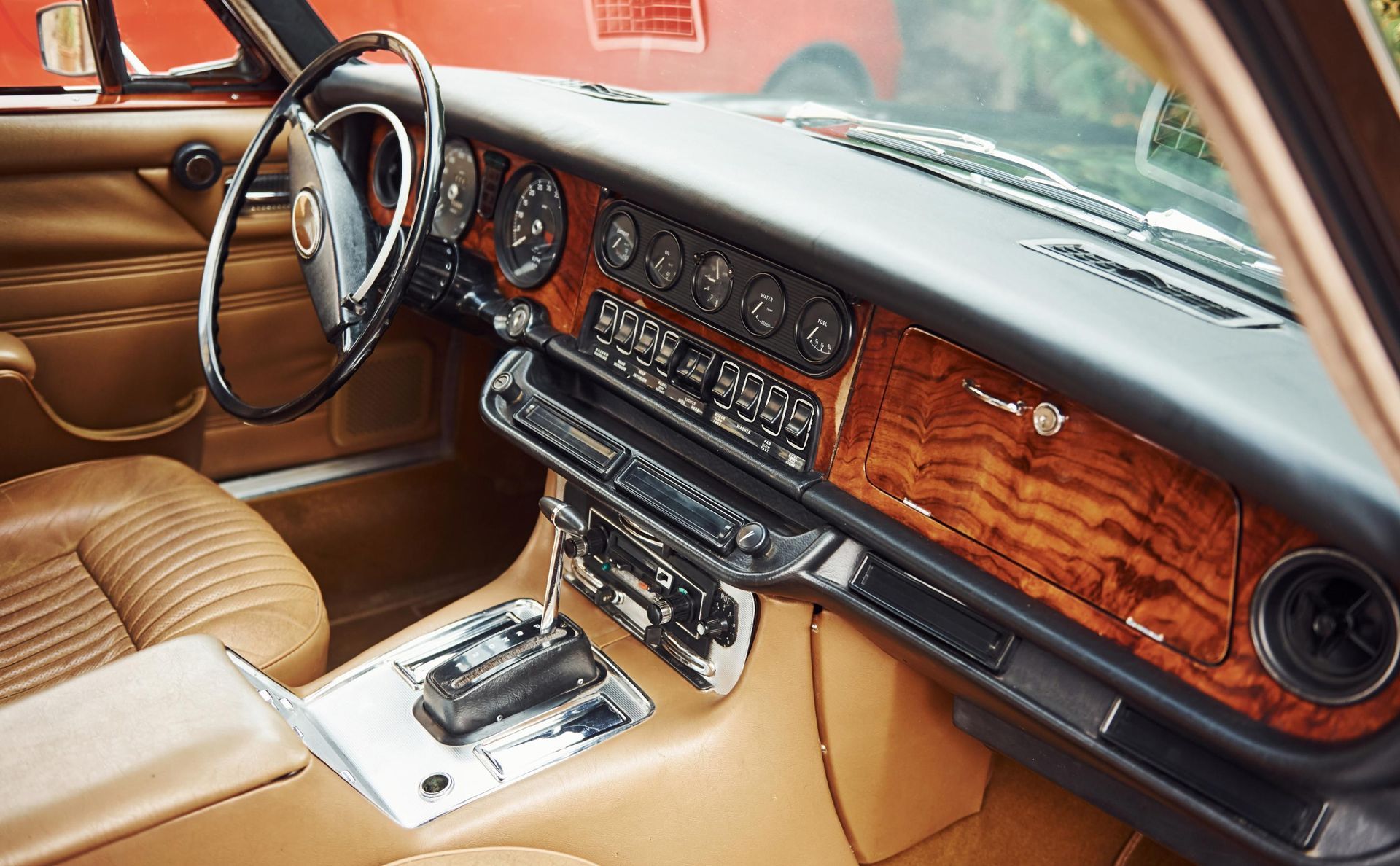 Interior view of a classic Jaguar with wood-paneled dashboard, tan leather seats, and chrome details.