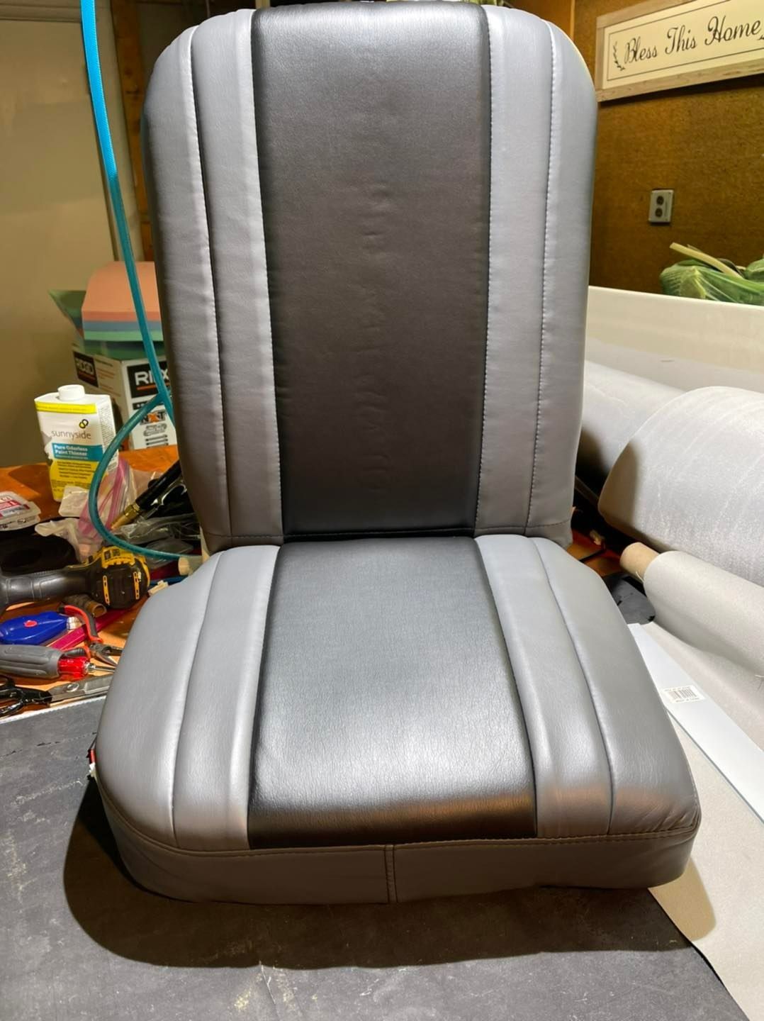 Gray and black car seat with a high back, in a workshop setting.