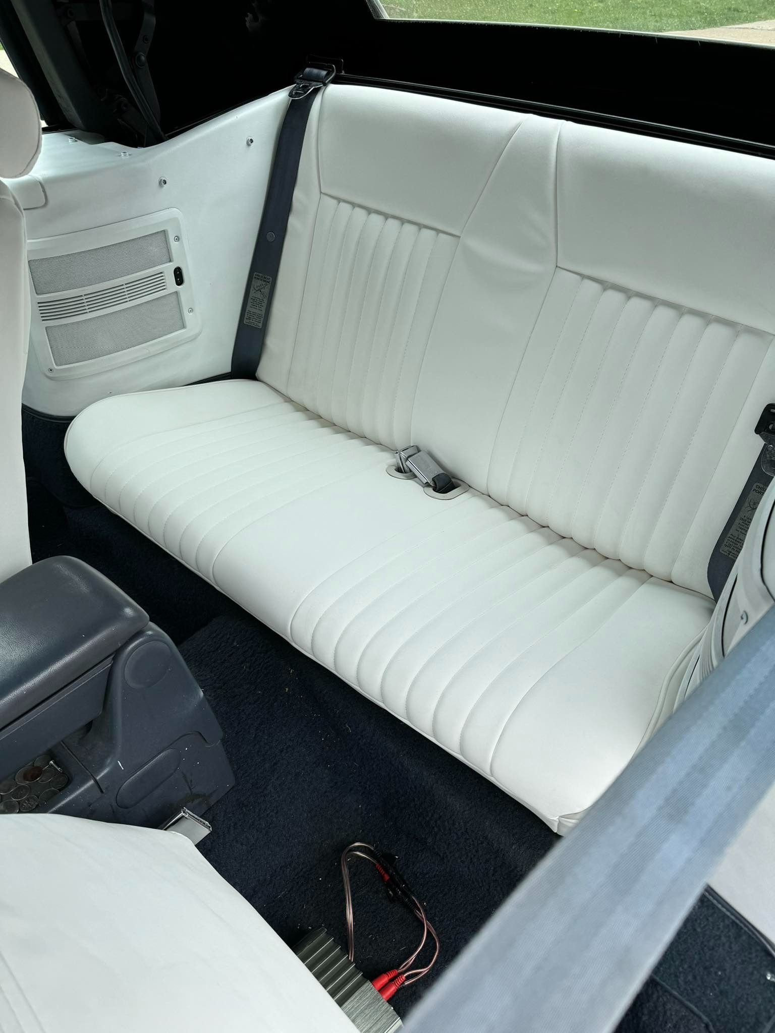 White leather car back seat with black trim and seatbelt.