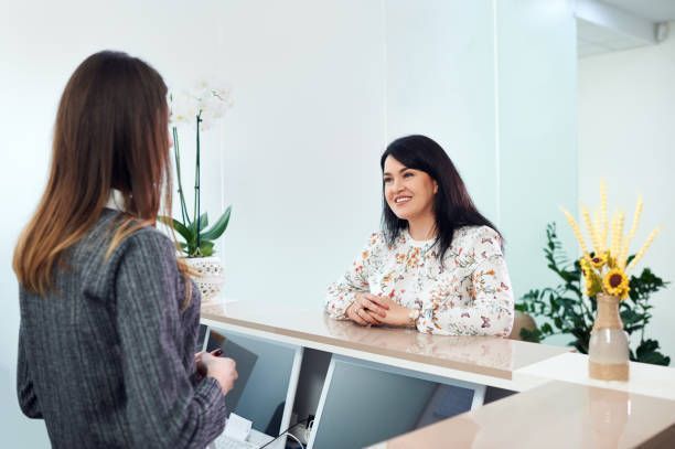A woman is sitting at a reception desk talking to another woman.