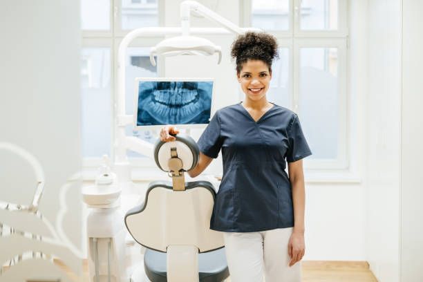 A female dentist is standing next to a dental chair holding an x-ray of a patient 's teeth.