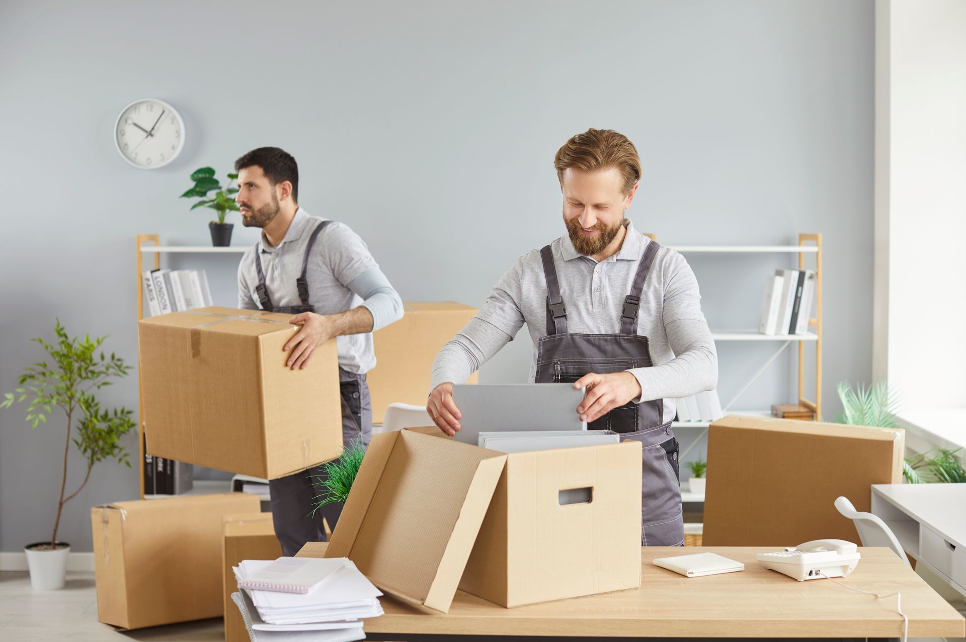 A pair of male movers handle several boxes for a moving, inside an office.