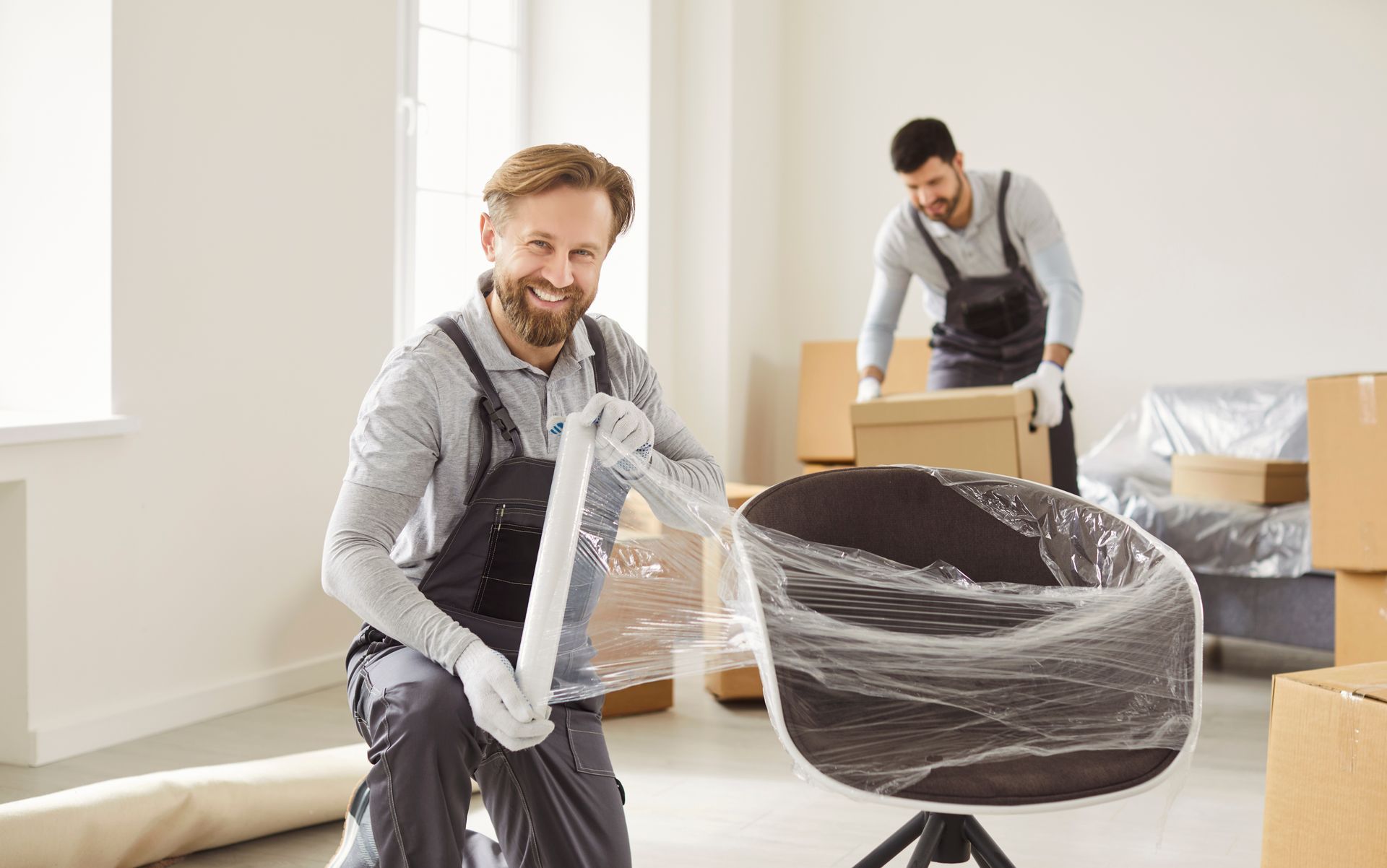 Two professional movers carefully handling wrapped furniture and boxes indoors. Two professional movers carefully handling wrapped furniture and boxes indoors.