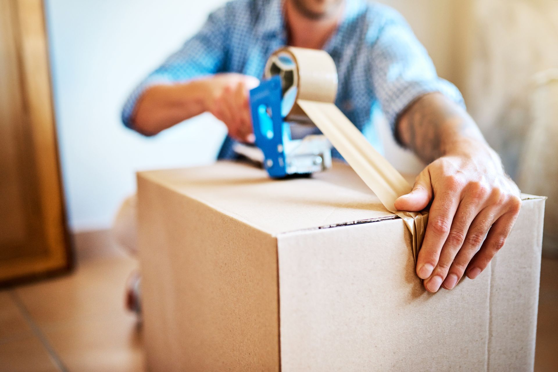 Person sealing cardboard box with packing tape, preparing package for shipping or moving service job.
