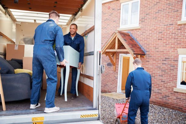 Moving company workers unloading furniture from truck into new home during residential relocation.