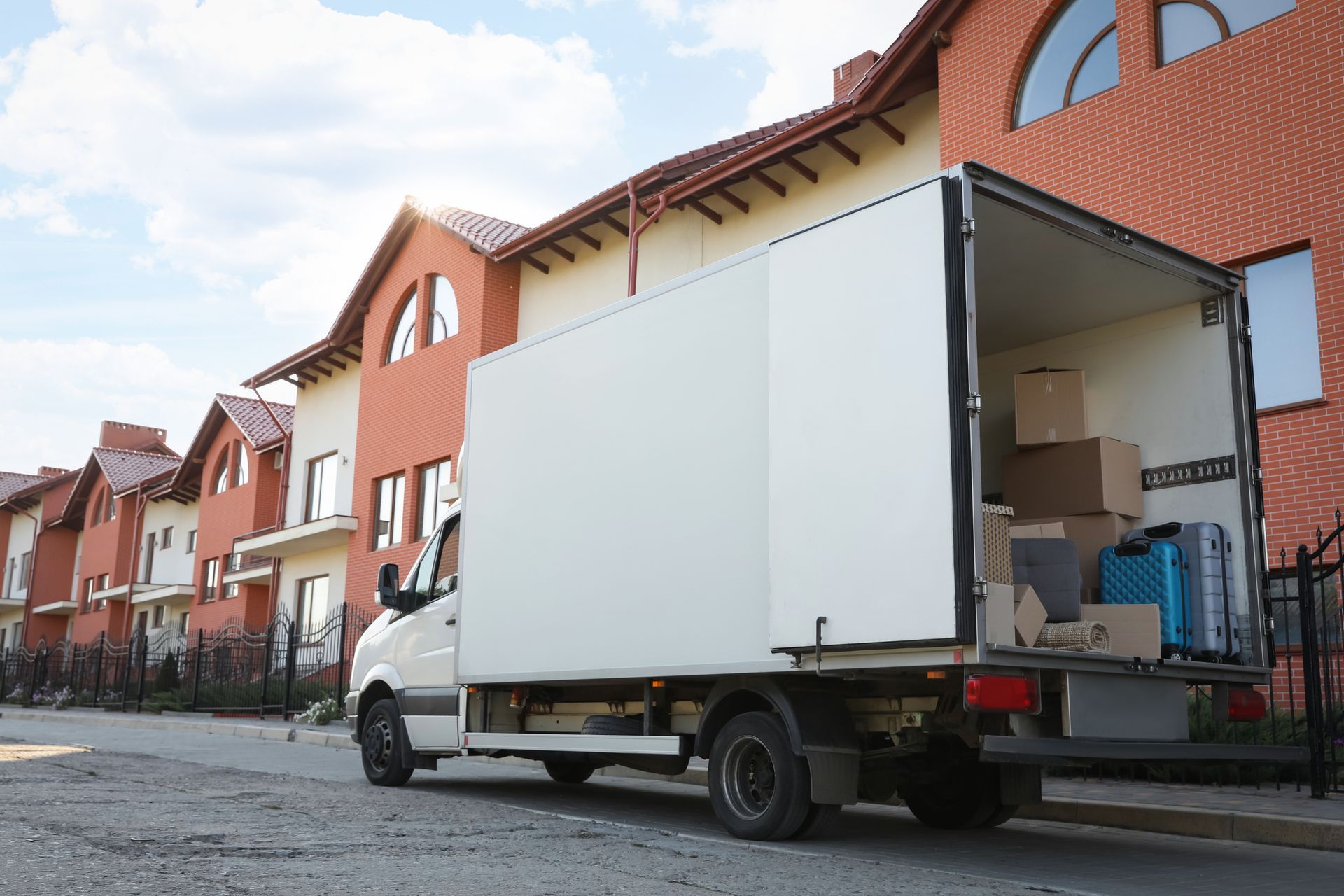 Moving truck with open door and boxes parked outside modern red-brick townhouses during relocation.