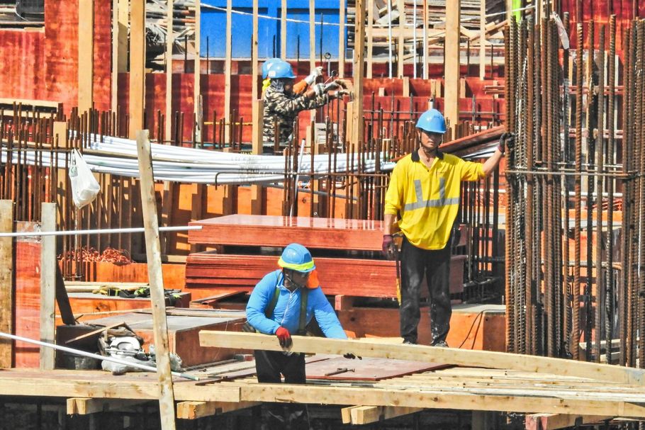 Construction workers in hard hats and safety gear working on a building frame with wooden forms and metal reinforcements.