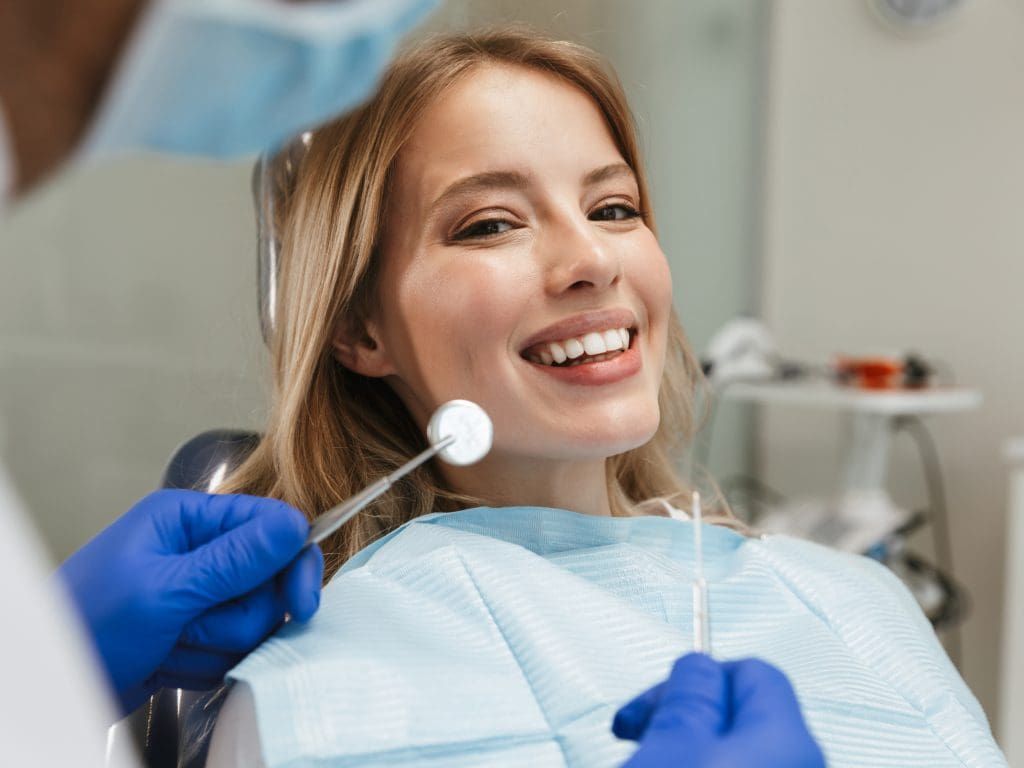 A woman is sitting in a dental chair while a dentist examines her teeth.