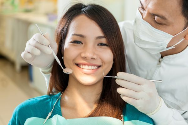 A woman is sitting in a dental chair while a dentist examines her teeth.