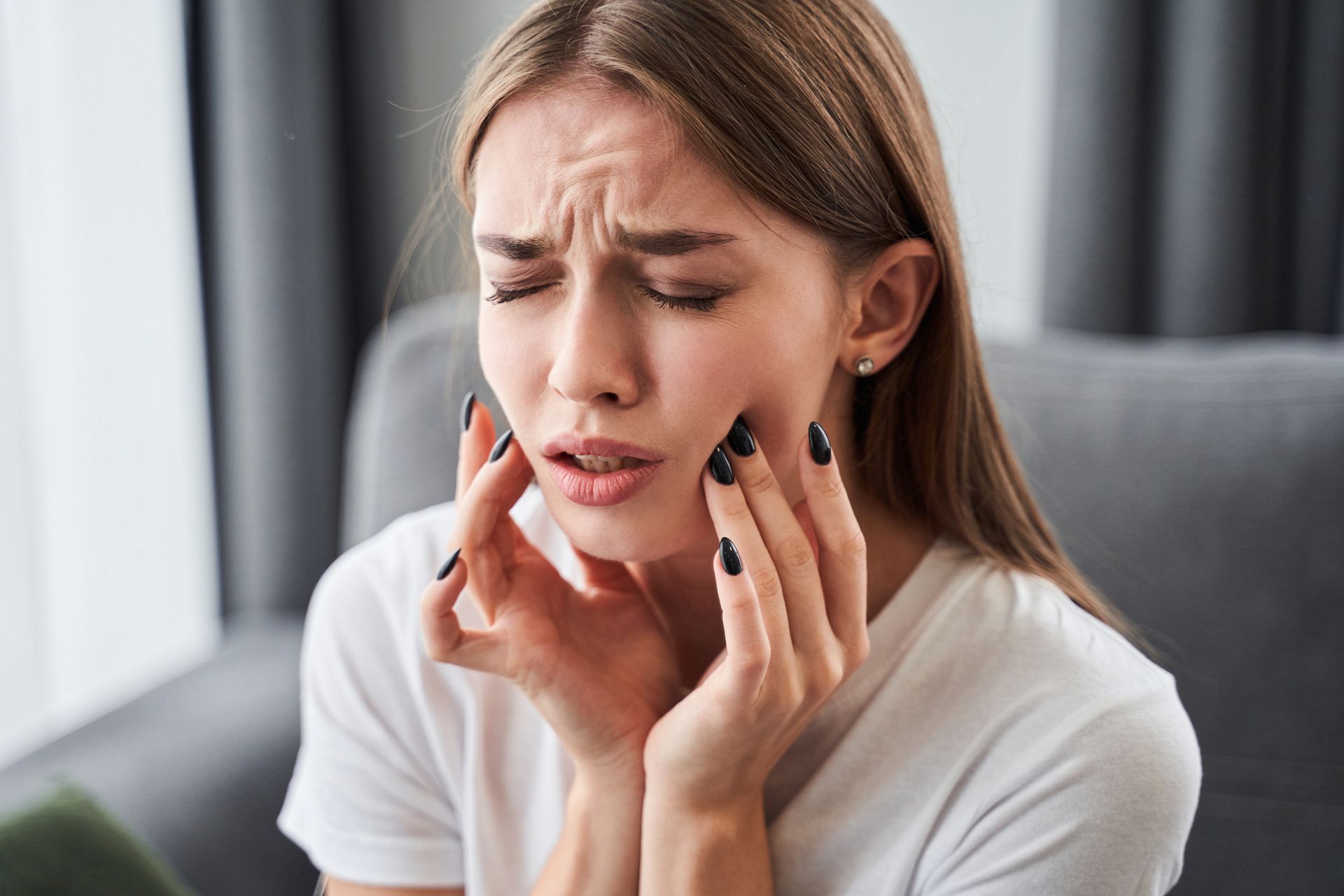 A woman is sitting on a couch with a toothache.