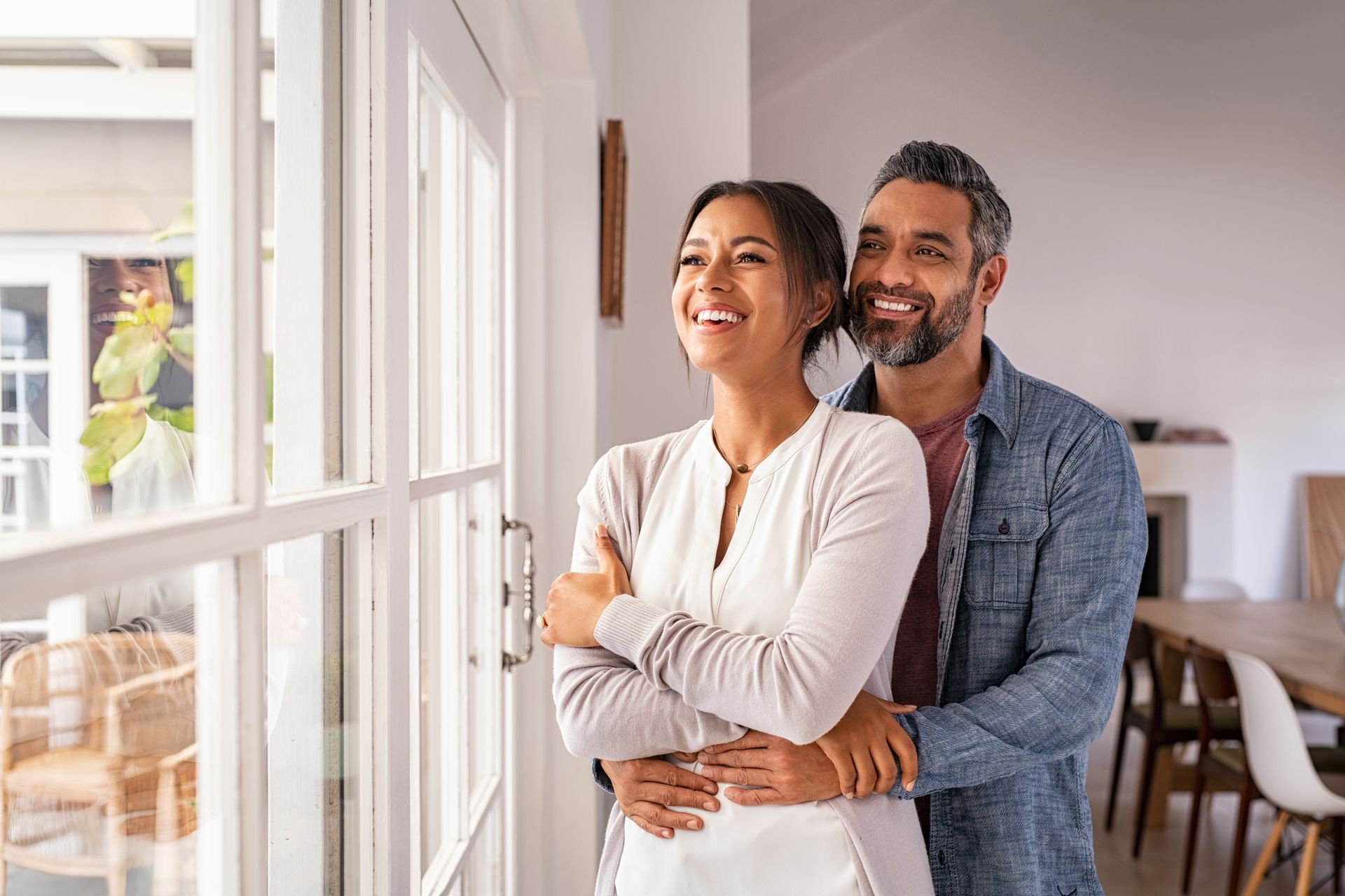A man and a woman are standing next to each other in front of a window.