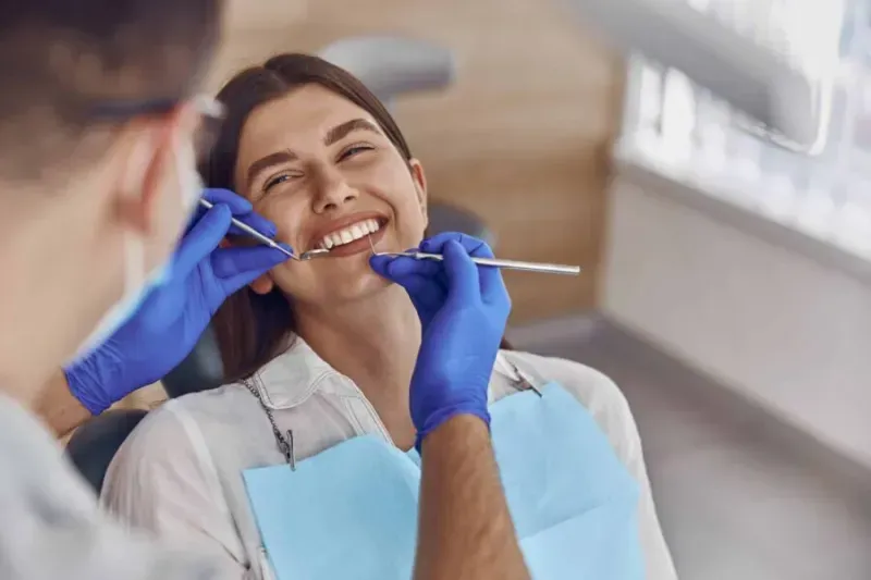 A woman is sitting in a dental chair while a dentist examines her teeth.