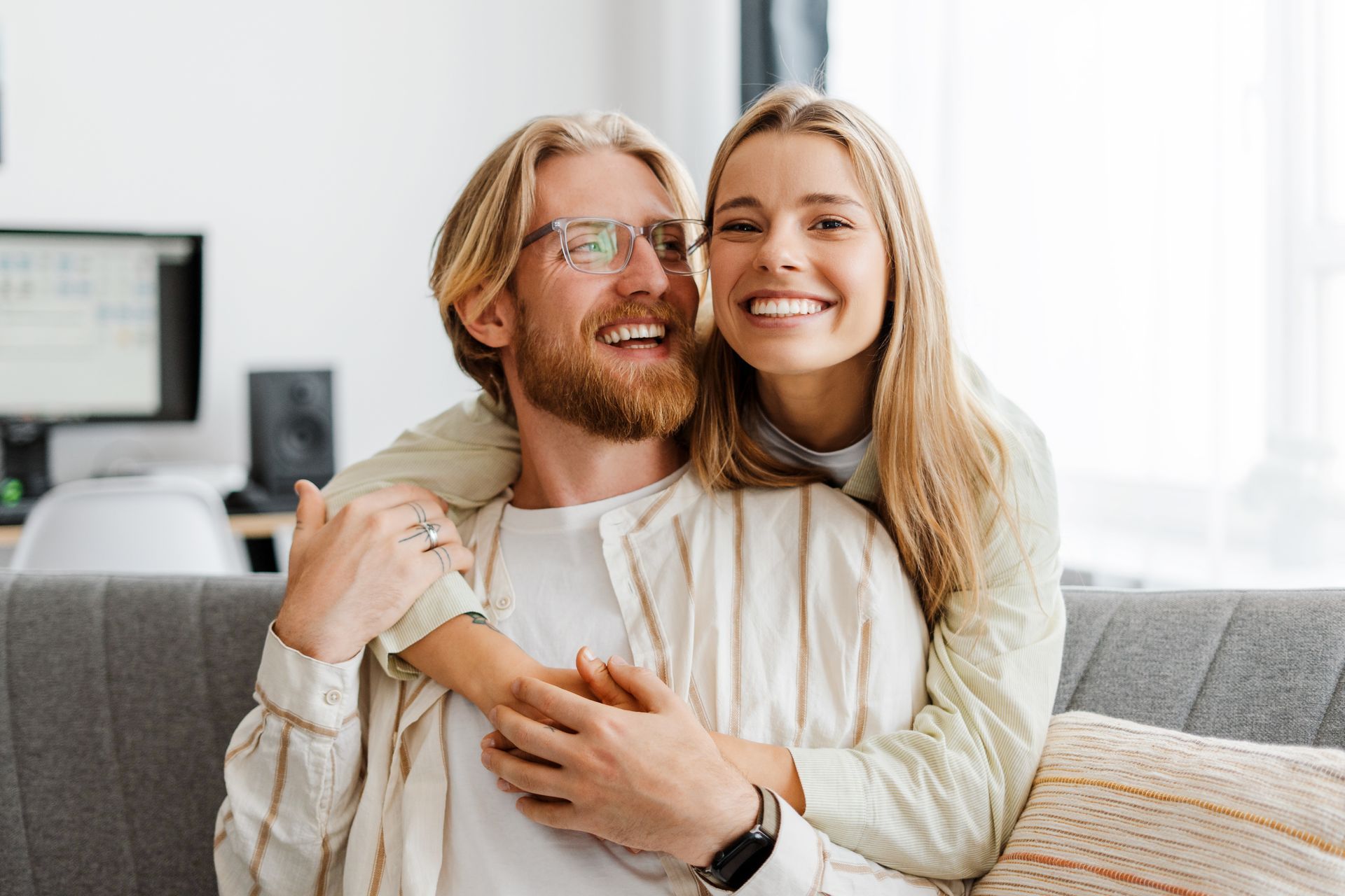 A woman is giving a man a piggyback ride while sitting on a couch.