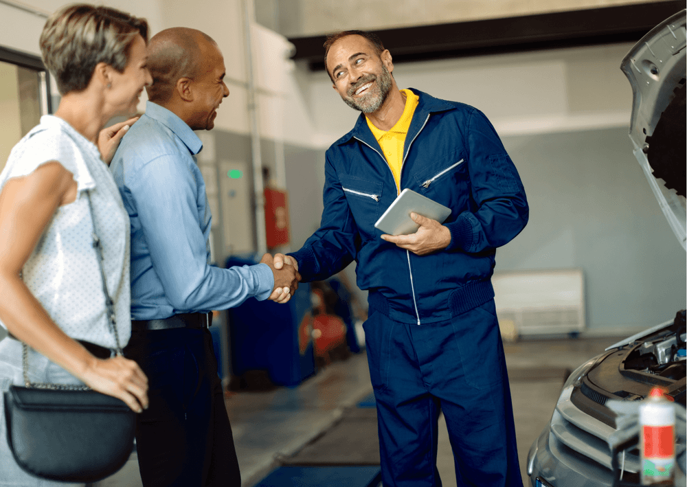 Mechanic shaking hands with a customer beside an open car hood in a garage