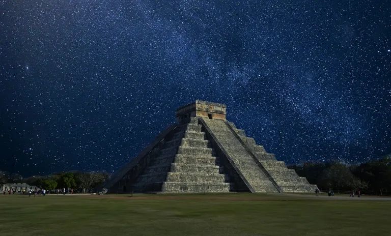 The pyramid is lit up at night with a starry sky in the background.
