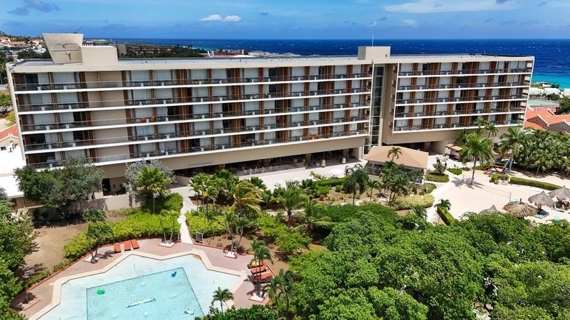 An aerial view of a hotel with a swimming pool in front of it.