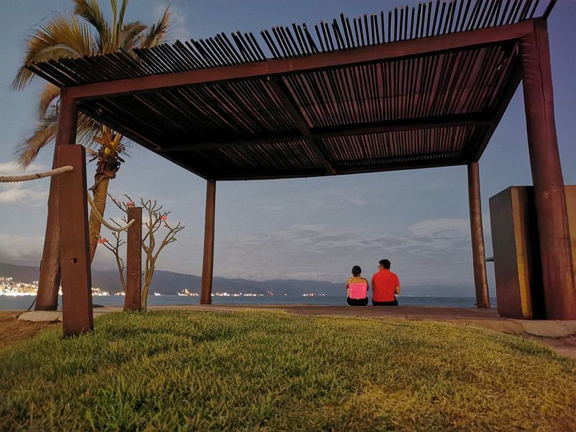 Two people sit under a wooden structure overlooking the ocean