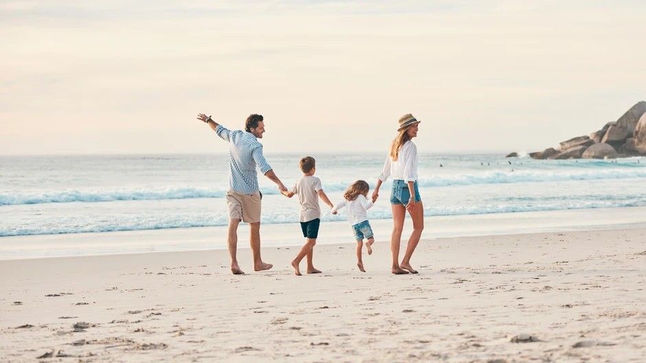 A family is walking on the beach holding hands.