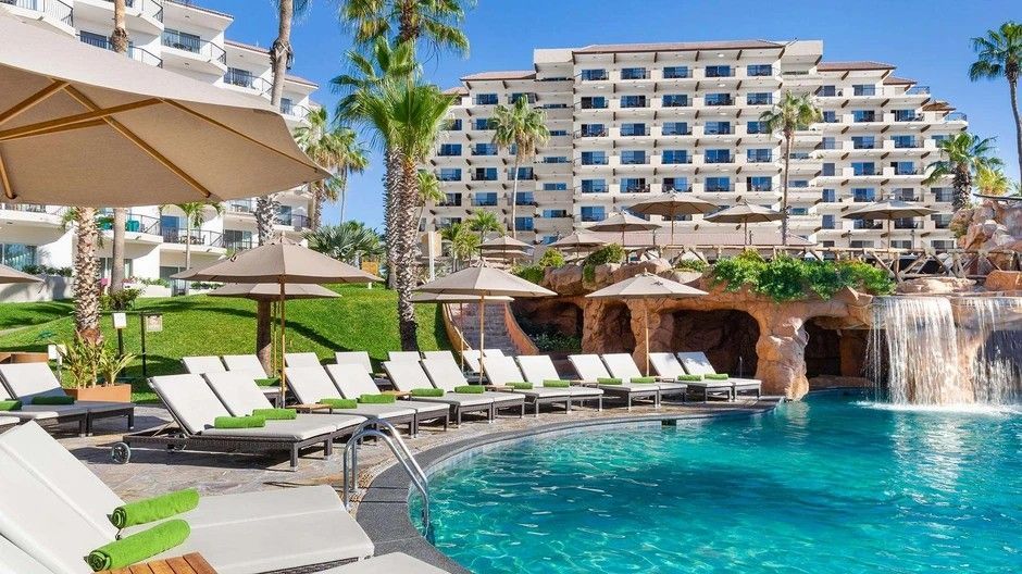 A large swimming pool surrounded by chairs and umbrellas in front of a hotel.