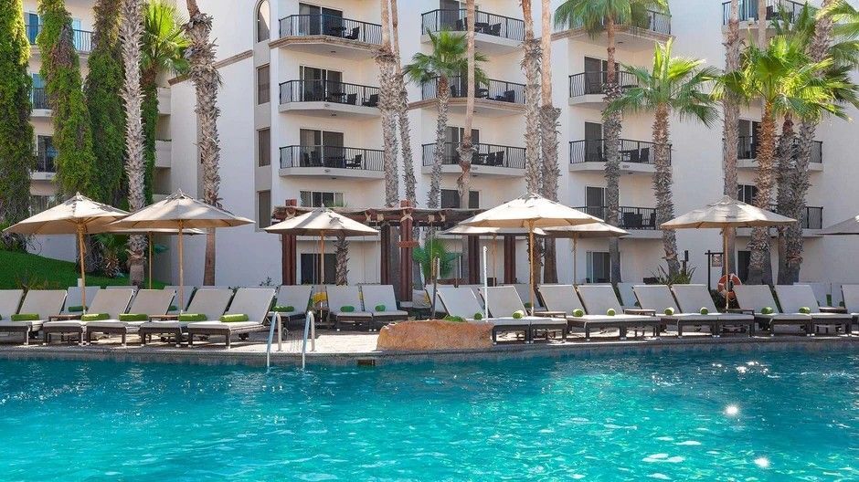 A large swimming pool surrounded by chairs and umbrellas in front of a building.