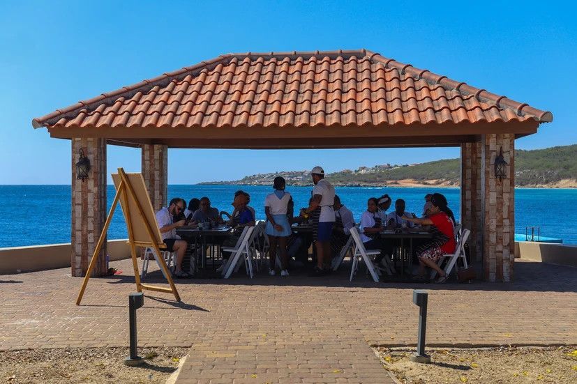 A group of people are sitting at tables under a gazebo overlooking the ocean.