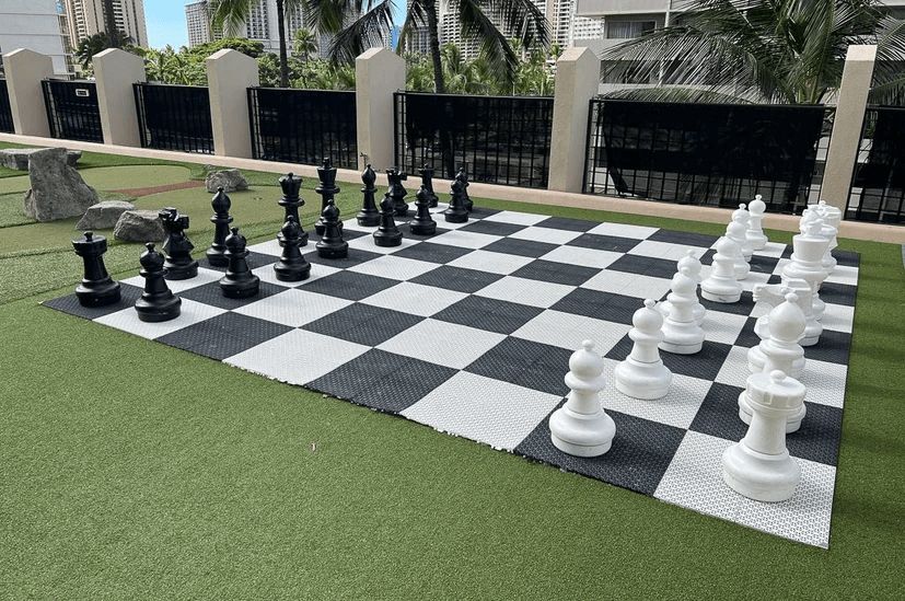 A large chess board is sitting on top of a lush green field.