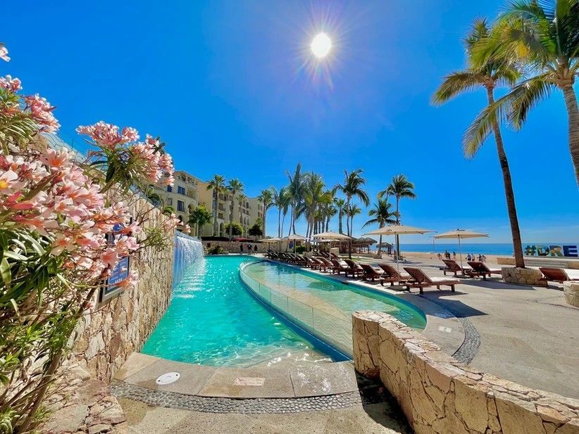 A large swimming pool surrounded by palm trees and chairs at a resort.