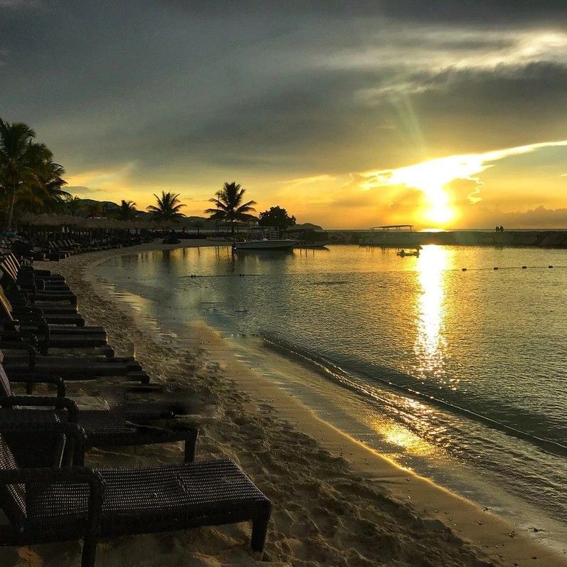 A beach with chairs and a sunset in the background