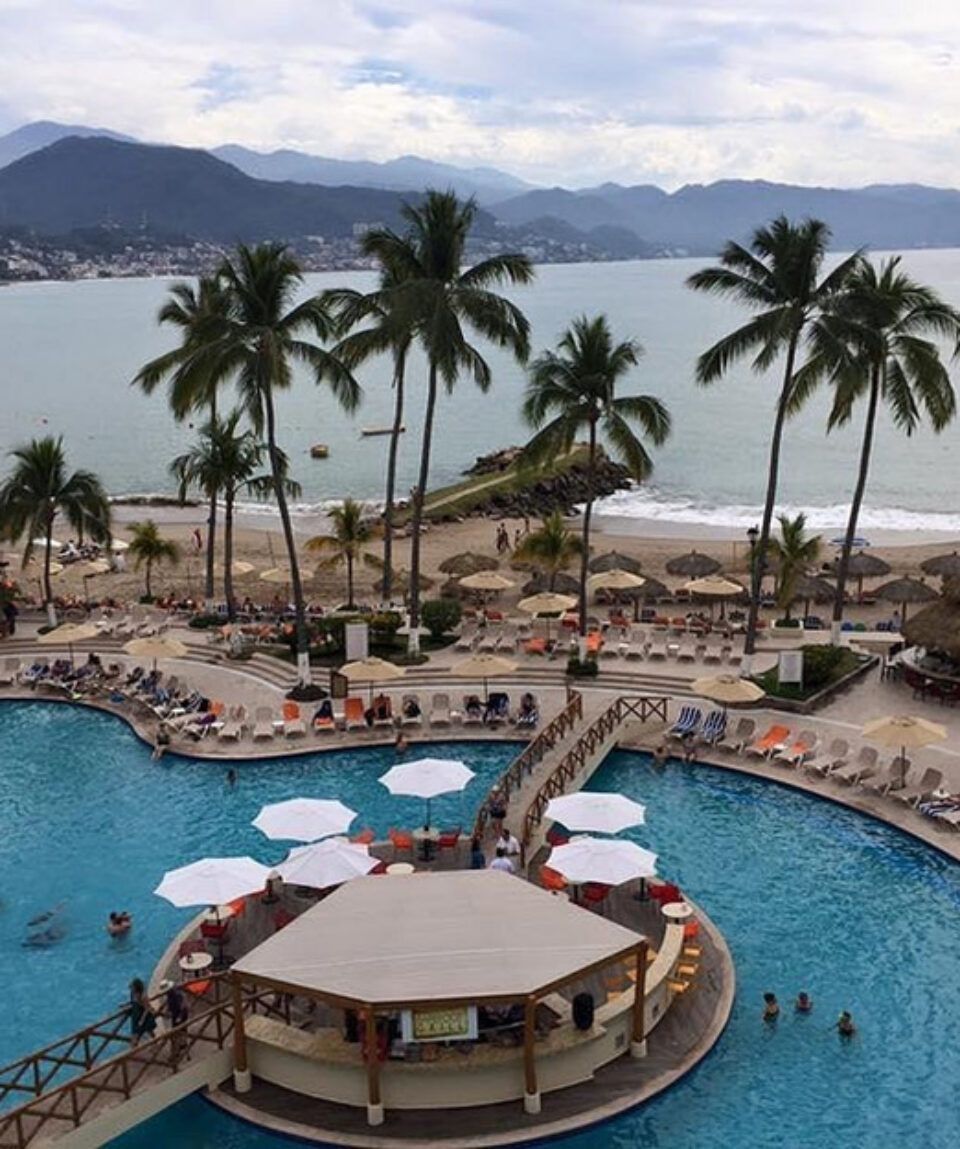 A large swimming pool surrounded by palm trees and umbrellas