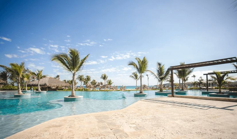 A large swimming pool surrounded by palm trees and a beach.