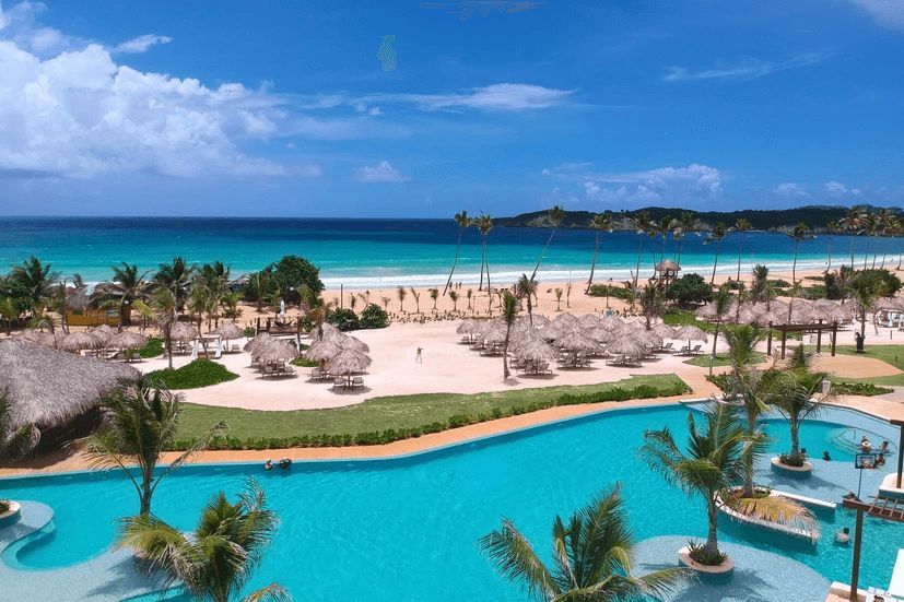 A large swimming pool surrounded by palm trees next to a beach.