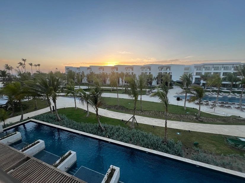 A large swimming pool surrounded by palm trees and a building at sunset.