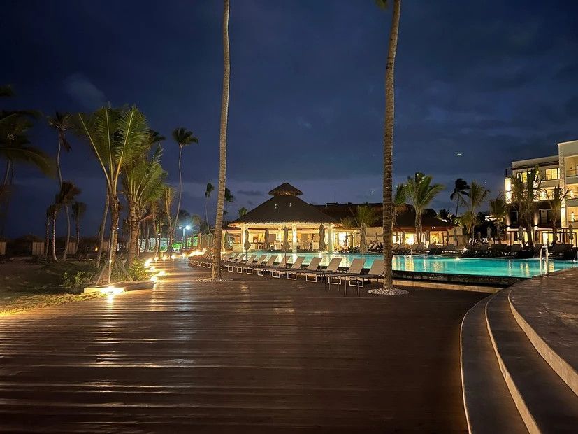 A large swimming pool is lit up at night in front of a hotel.